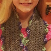 A girl with a brown crocheted scarf with a scallop patten.