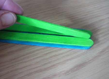 place the stick on edge between the two green sticks