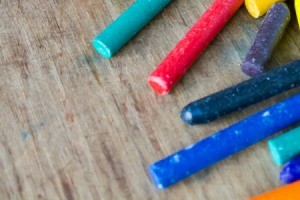 Several unmarked crayons laying on unfinished wood surface.  There are crayon marks on the wood.