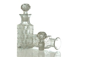 Two clear cut crystal decanters on a white background.  One is upright with stopper inserted.  The other is on it's side with it's stopper laying next to it.