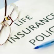 White paper with "LIFE INSURANCE POLICY" in bold typeface.  A folded pair of glasses and a pen rest on the paper.
