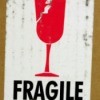 Red image of broken glass and the word FRAGILE in black on a white label against a cardboard box background.