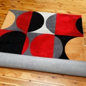 Brightly colored black, red, grey, yellow, and white area rug partially unrolled on a wood floor