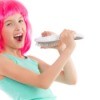 Young girl wearing hot pink wig singing into hairbrush against a white background