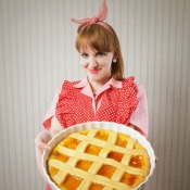 Woman in red checked apron holding homemade lattice crust pie