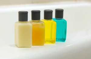 Four small bottles like those you would get of shampoo, conditioner, and lotion at a hotel, lined up on the edge of a tub.