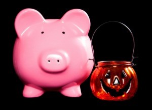 A piggybank next to a Halloween pumpkin candle holder.