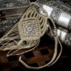 Intricate macrame (finger weaving) necklace resting against silver or pewter boxes on a dark wood surface.