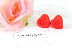 Close-up of large desk calendar with March 13th marked as Wedding with two red hearts and a large pink roses laying on the calendar.