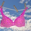Hot pink bra with small yellow and white flowers hanging from a clothesline against a background of blue sky and clouds