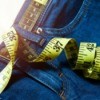 Close-up of a pair of jeans with a measuring tape curled on top and through the belt loop against a wooden background
