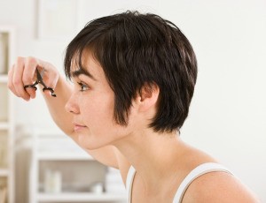 A woman with a short pixie cut and long sideburns trims her bangs