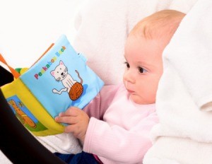 Baby in pink sweater in a car seat "reading" a fabric book