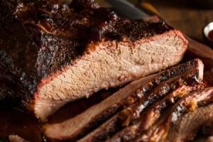 Close up of beef brisket partially sliced on a wooden cutting board