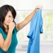 Woman holding blue shirt in hand with a look of obvious disgust and her other hand plugging her nose.