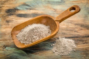 Wooden scoop holding buckwheat flour against a faded wooden surface