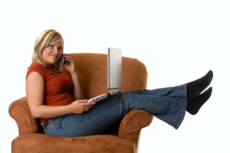 Woman with laptop and phone sitting across a rust colored armchair.