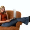 Woman with laptop and phone sitting across a rust colored armchair.
