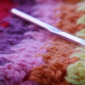 Crochet hook resting on striped crocheted blanket