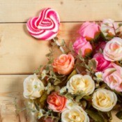 Bouquet of roses with a decorative candy striped red heart on a stick against wooden background