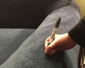 Child's hand holding the point of a Sharpie permanent marker to a microfiber couch