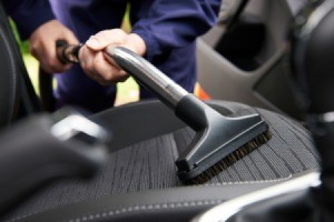 Close up of a vacuum wand with upholstery attachment vacuuming a car seat.