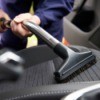 Close up of a vacuum wand with upholstery attachment vacuuming a car seat.