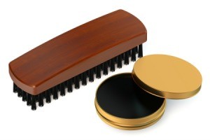 Opened tin of black shoe polish and a brush against a white background