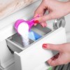 Hand pouring powdered laundry detergent into washing machine using pink scoop