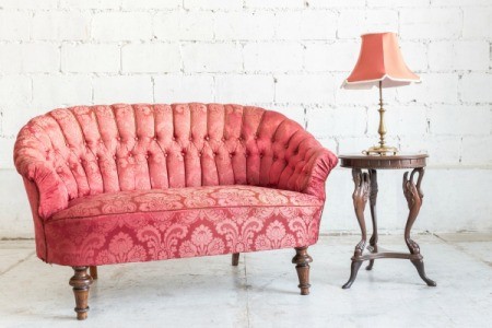Rose pink vintage couch with wooden side table and table lamp with rose pink shade against white brick background