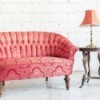 Rose pink vintage couch with wooden side table and table lamp with rose pink shade against white brick background