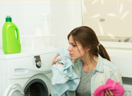 Woman crouched in front of a front loading dryer smelling a shirt