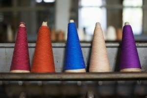 Five thread cones with different colors of thread lined up on a shelf