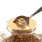 Spoon breaking through gold colored foil on a plastic coffee container