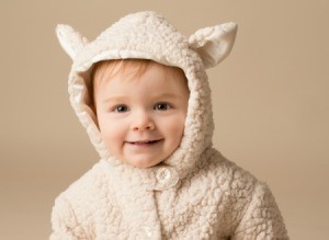 Smiling baby in a Lamb Costume against a beige background