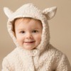 Smiling baby in a Lamb Costume against a beige background