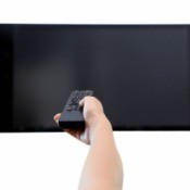 Hand holding remove pointing to flatscreen TV that is turned off