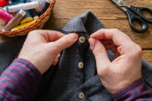 Man's hands sewing button on shirt