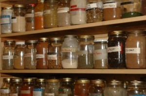 Wide variety of different types and sized of jars filled with spices on three shelves all with different types of labels