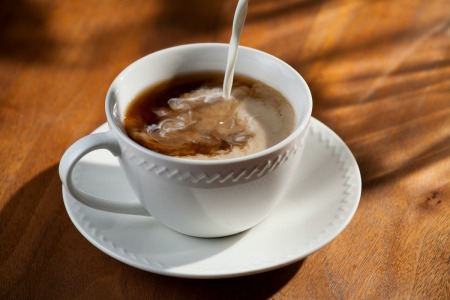 Liquid creamer being poured into white coffee cup on a table