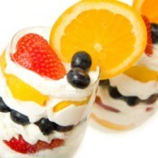 Two fresh fruit parfaits - lawyes or oranges strawberries and blueberries alternating with cream in a glass.