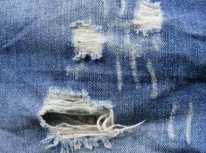 Close up image of a pair of jeans with rips, runs, and shredded areas