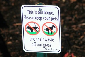 Close up of sign reading, "This is our home  Please keep your pets and their waste off our grass."