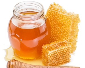 Jar of honey, two honeycomb, and spilled honey against a white background