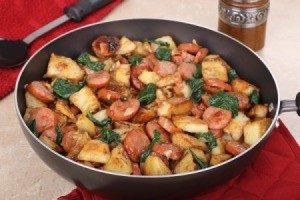 Skillet containing fried sausage and potatoes with onions and greens