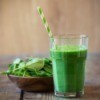 Green smoothie next to a bowl of fresh spinach leaves on a wooden table