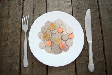 Pile of coins on a white plate with a knife and fork on a wooden table