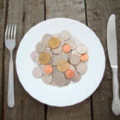 Pile of coins on a white plate with a knife and fork on a wooden table