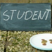Chalkboard with the word student written on it leaning against a wall behind a plate containing a few coins.