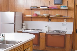 Basic 1970s era kitchen with old appliances and plats on a shelve along the wall